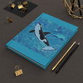 Notebook with an orca whale design on a dark surface with stationery items.