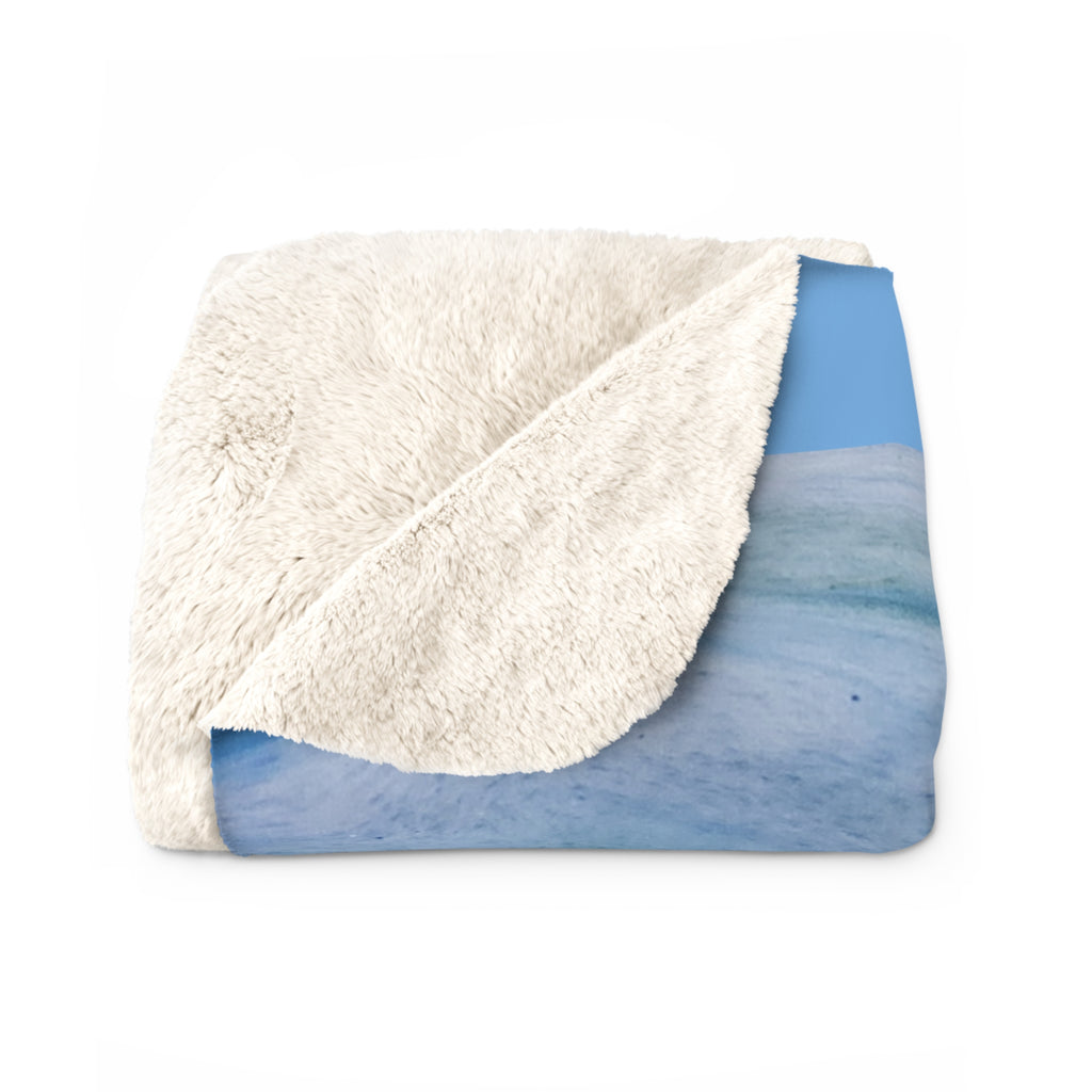 Folded blanket with white sherpa side and blue watercolor pattern on a white background