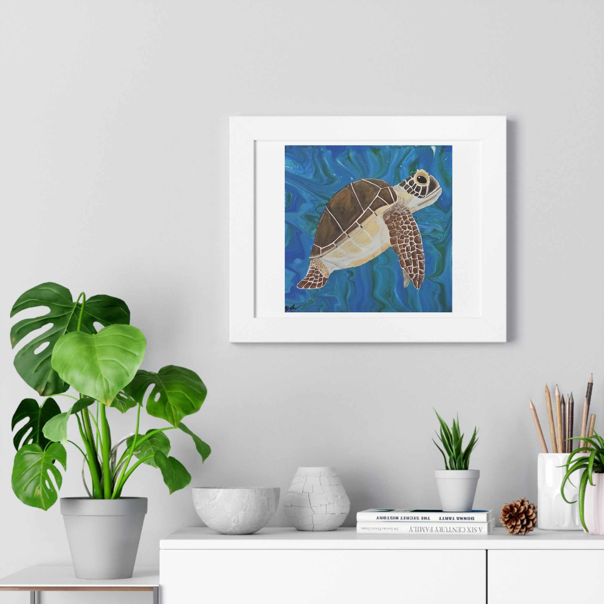 Framed artwork of a turtle on a wall above a desk with plants and decor.