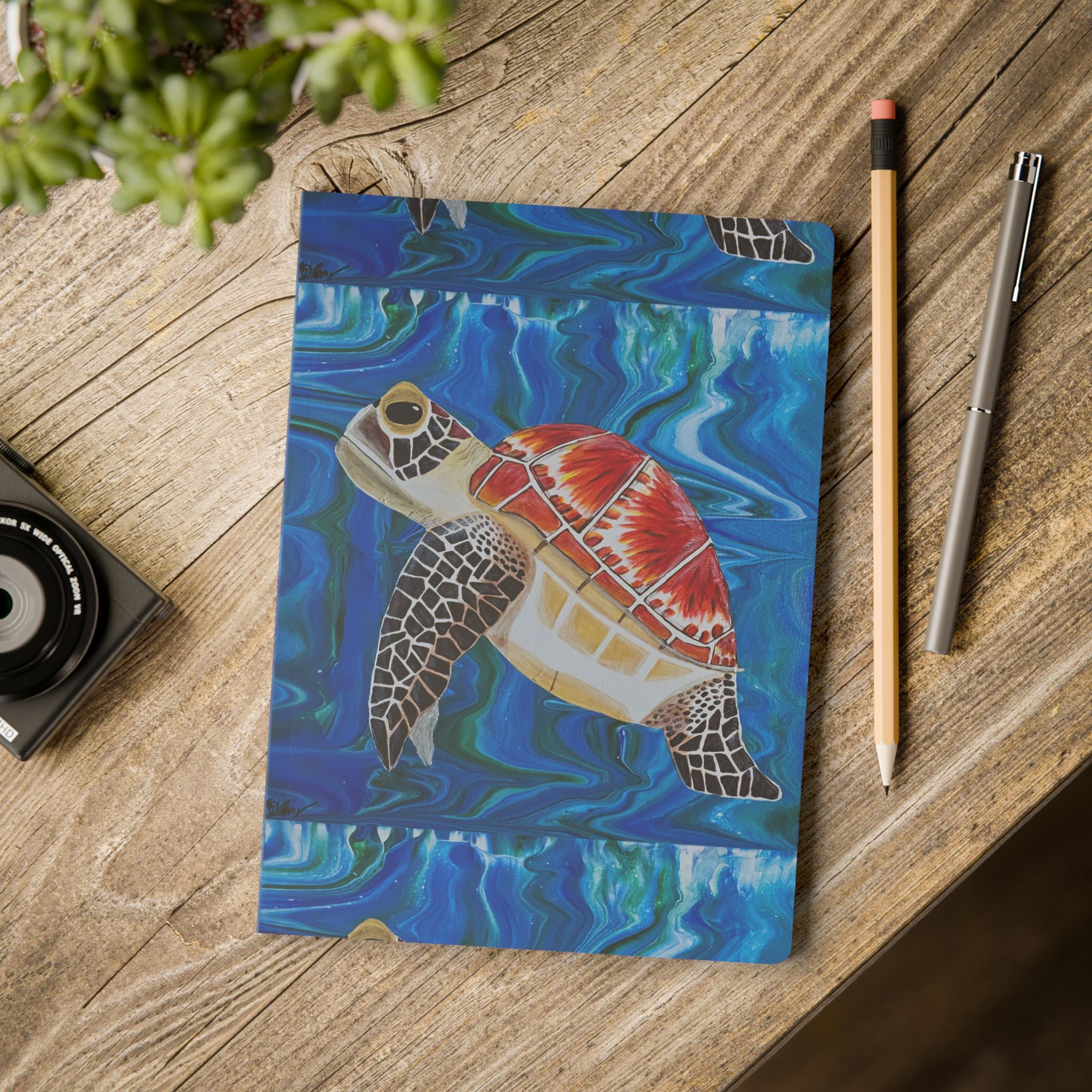 Notebook with a turtle design on a wooden surface with stationery items.