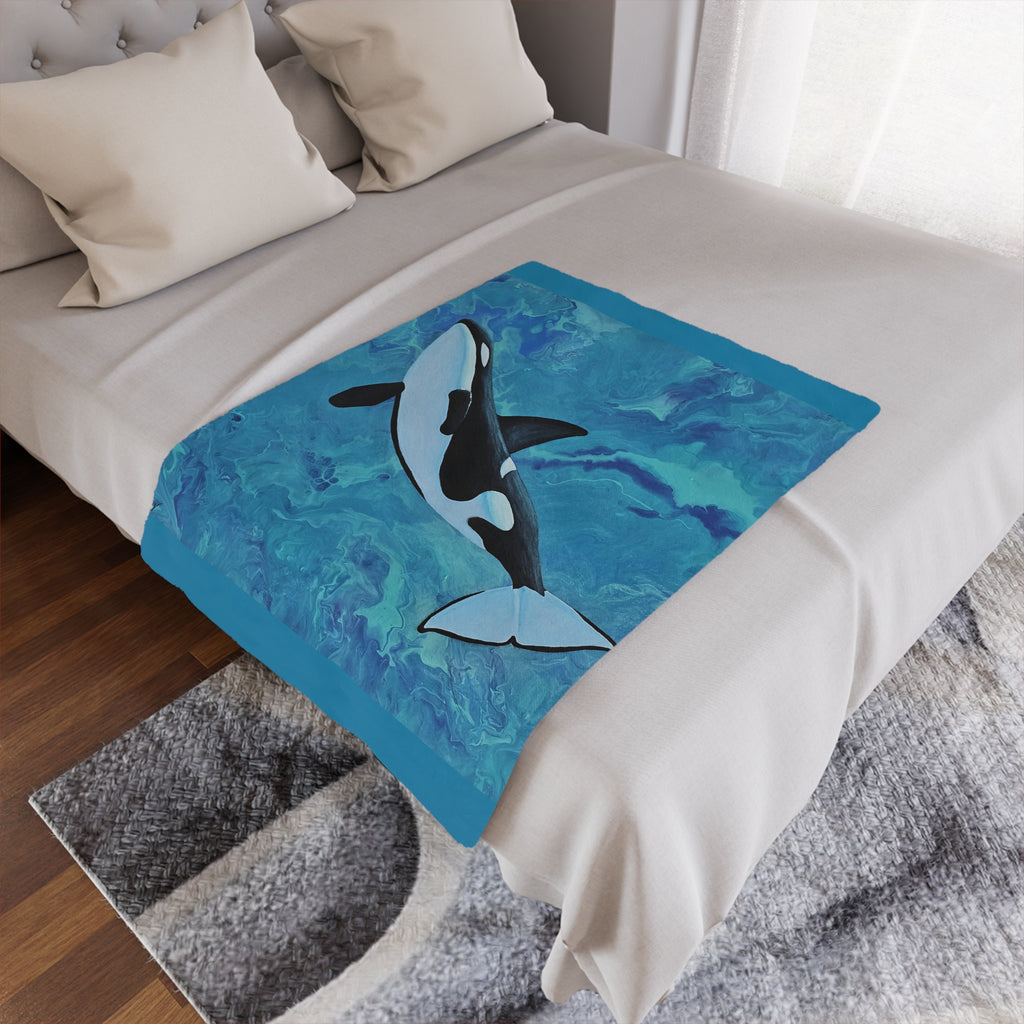 Bed with a decorative throw blanket featuring an orca whale design on a blue watercolor background.