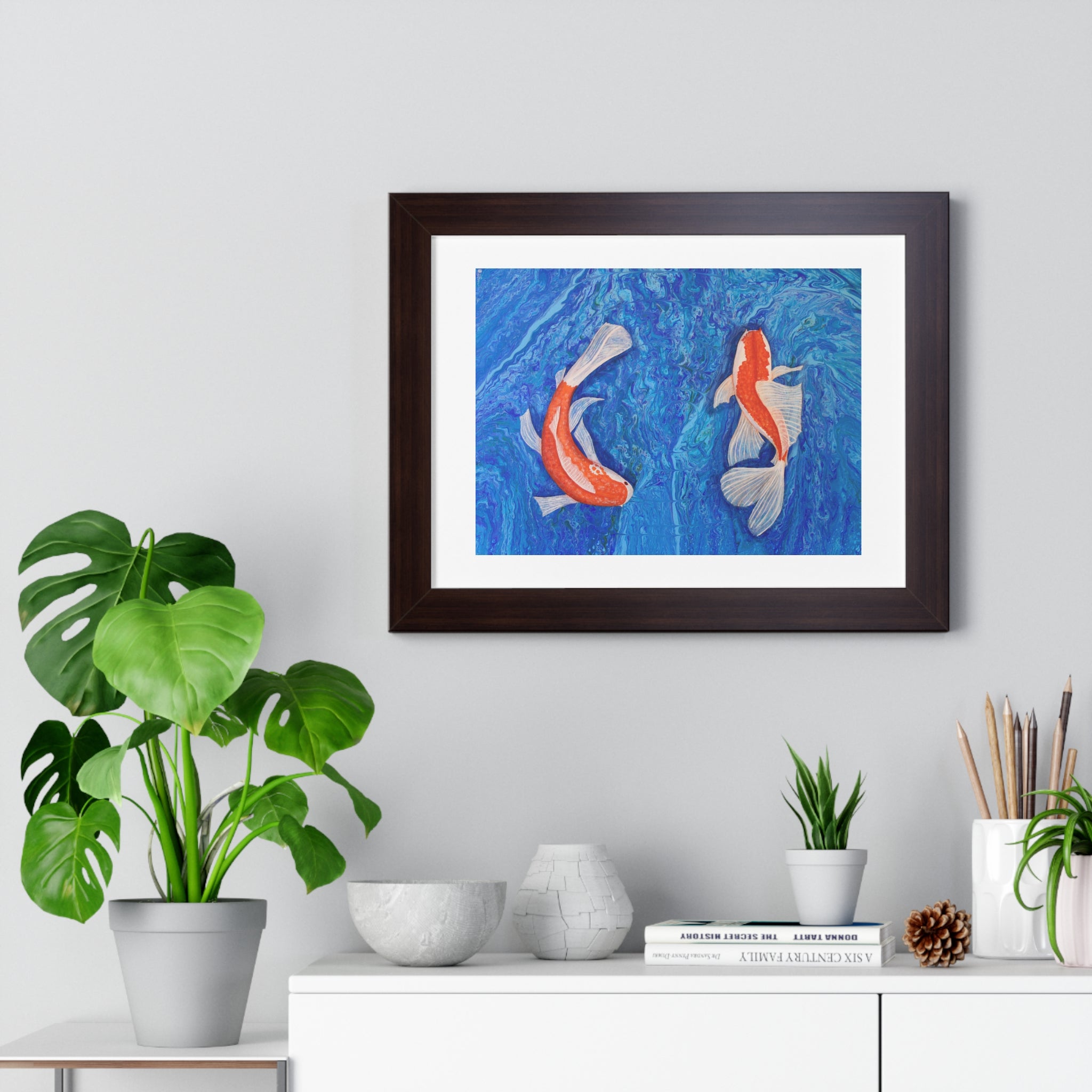 Framed artwork of two koi fish on a blue background, displayed in a room with plants and decor.