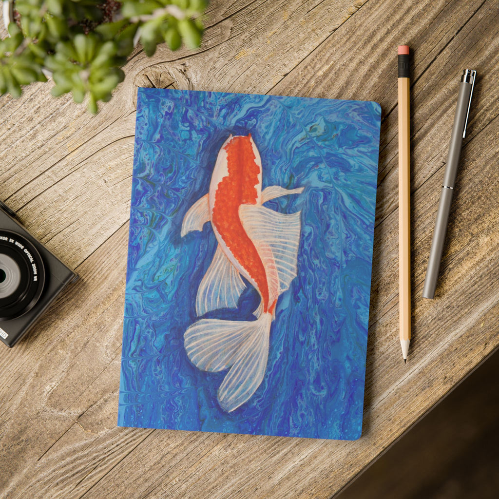 Notebook with a koi fish illustration on a wooden surface with stationery items.