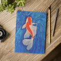 Notebook with a koi fish illustration on a wooden surface with stationery items.