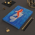 Notebook with a Koi fish design on a dark surface with office supplies.