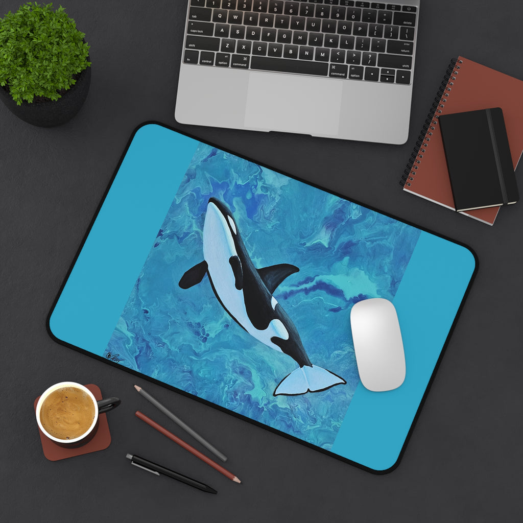 Desk setup with a desk pad featuring an orca whale design, laptop, notebook, and coffee cup.