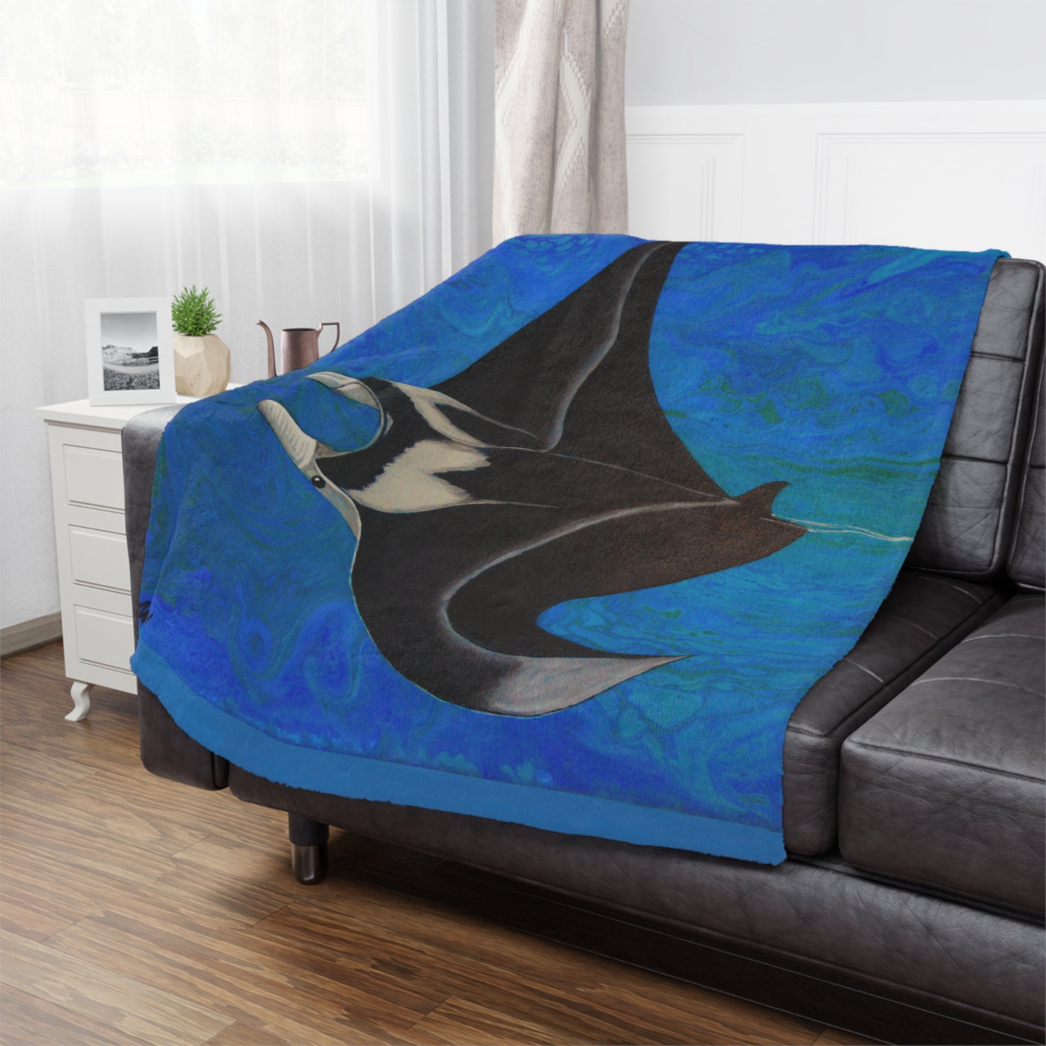 Blue blanket with a manta ray design draped over a black sofa in a living room.