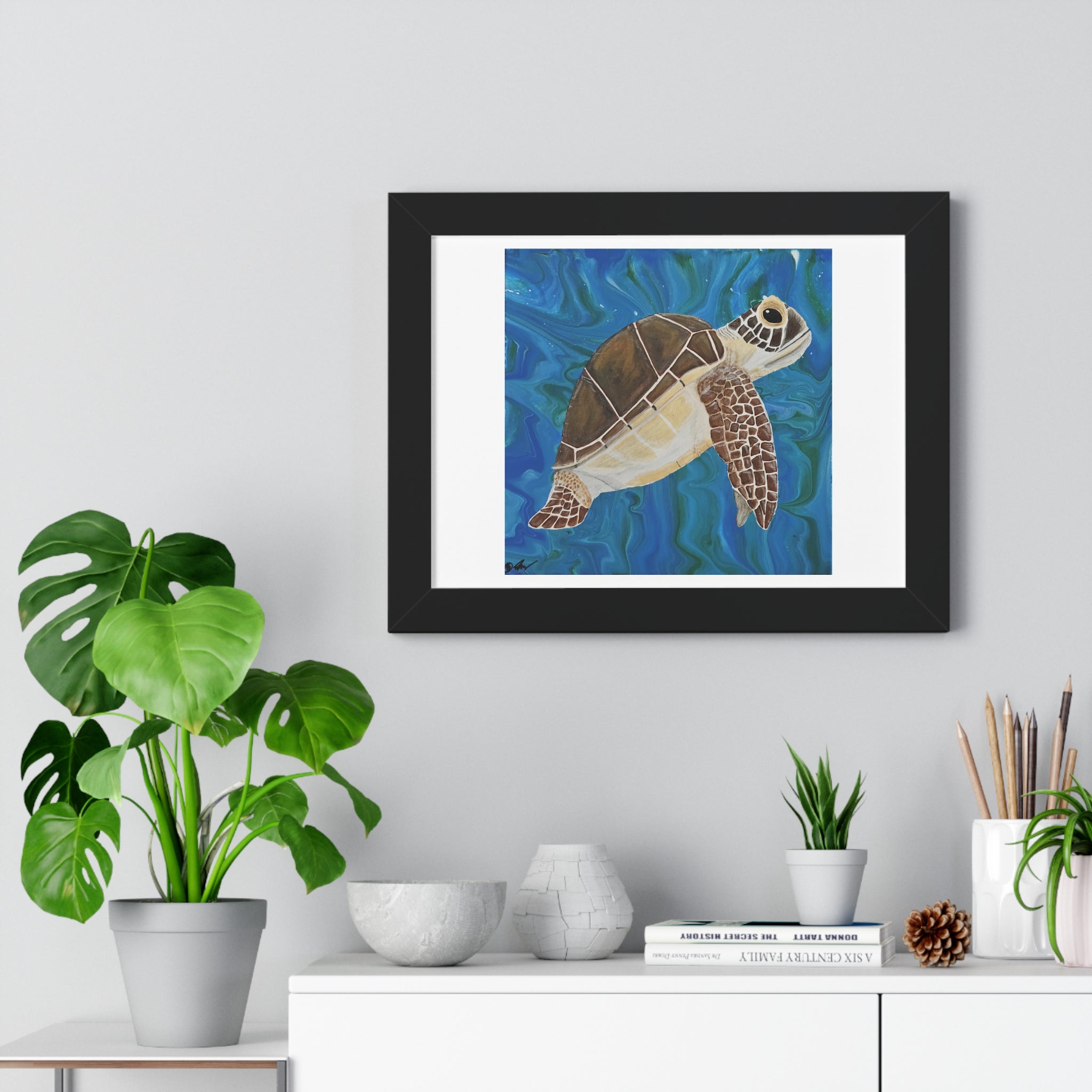 Framed artwork of a turtle on a wall above a white cabinet with decorative items.