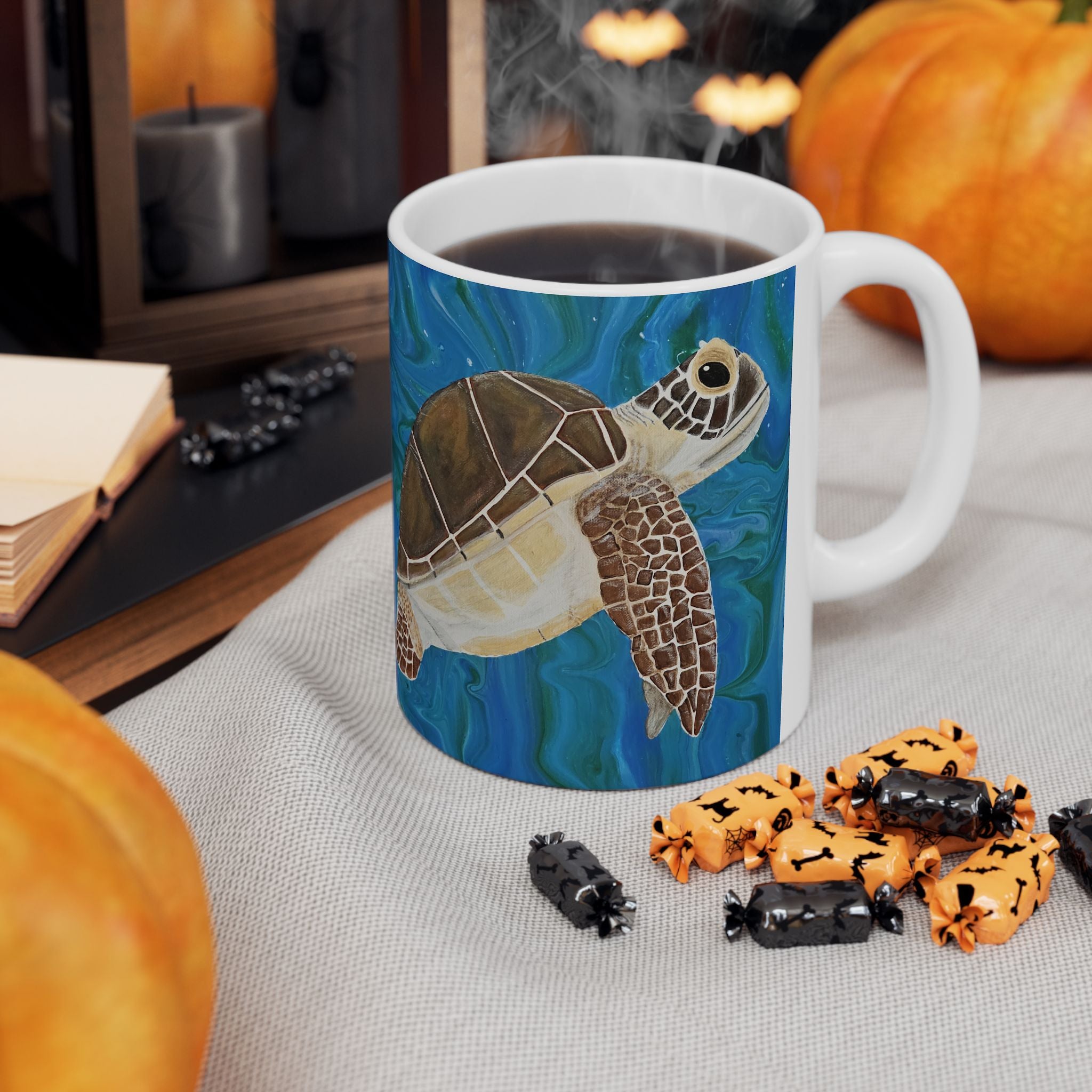 Mug with a turtle design on a table with Halloween-themed treats and pumpkins.