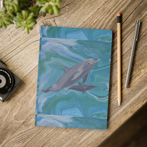 Notebook with dolphin illustration on a wooden surface with stationery items.