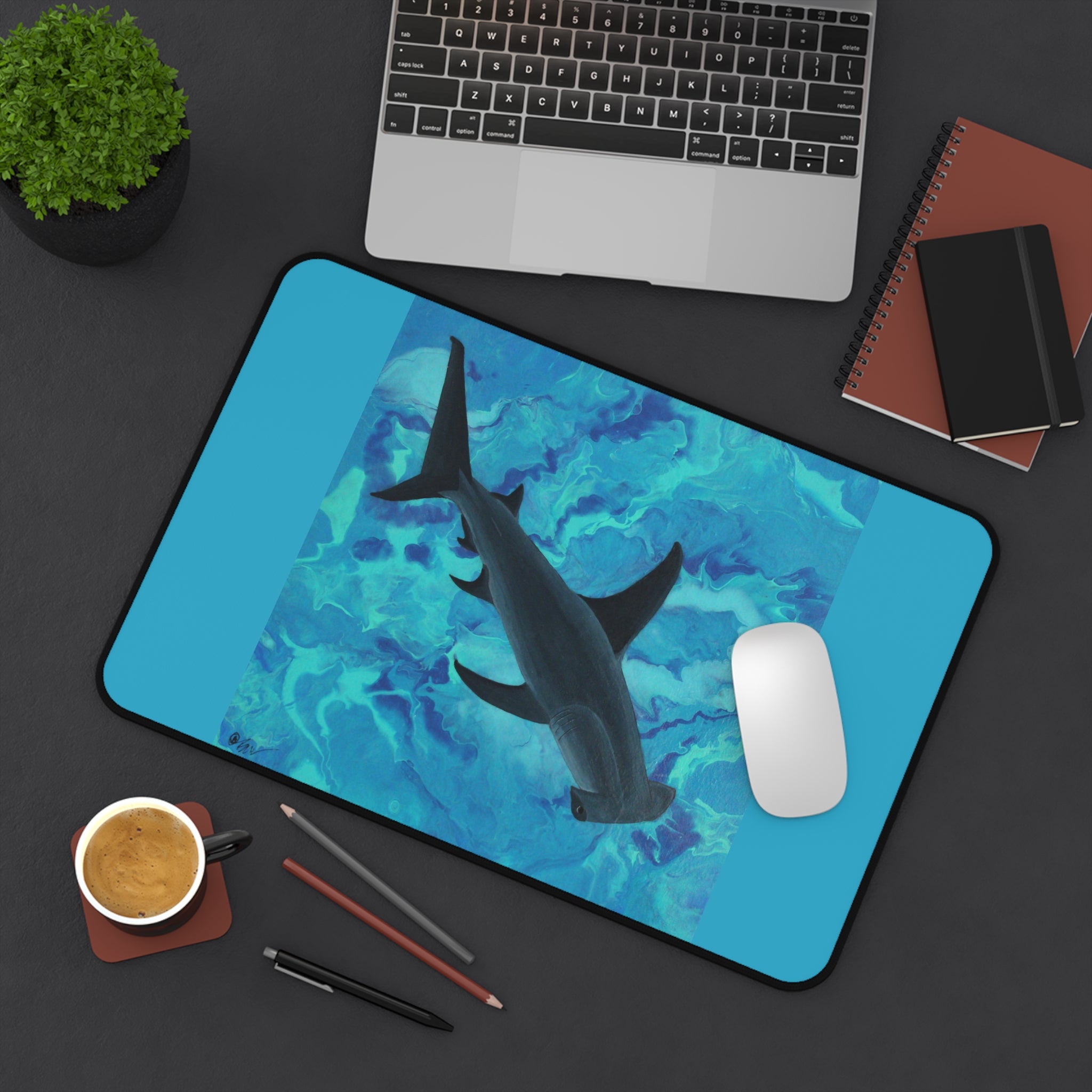 Desk setup with a shark design desk pad, laptop, and office supplies on a dark surface.