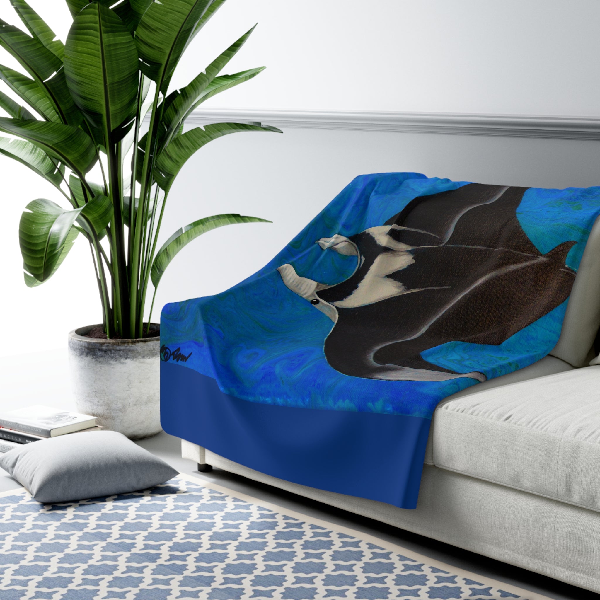 Couch with a manta ray blanket draped over it, next to a potted plant in a living room setting.