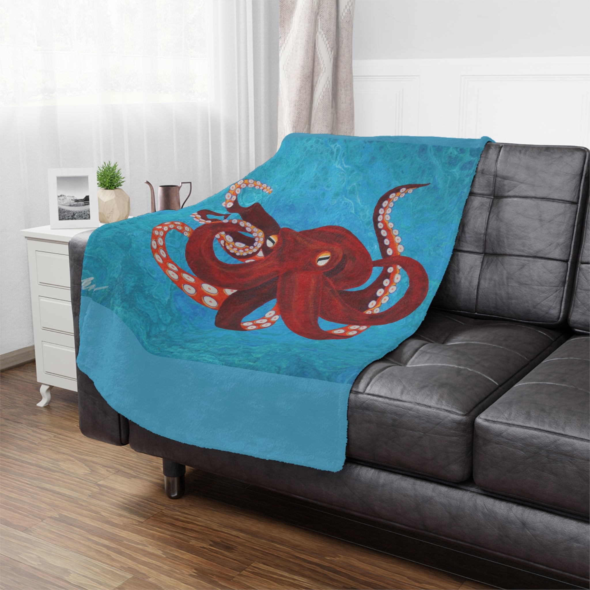 Blue blanket with a red octopus design draped over a gray sofa in a living room.