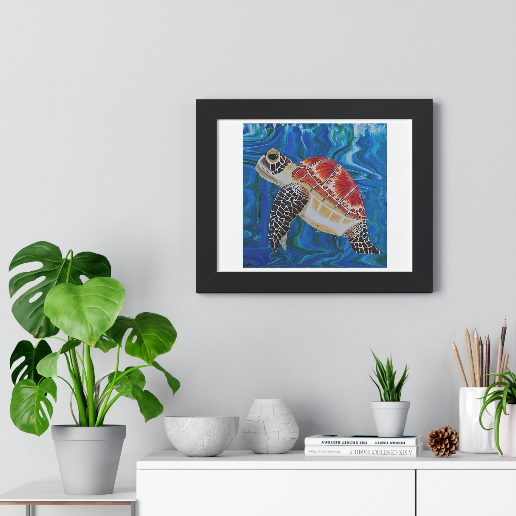 Framed artwork of a turtle on a wall above a white cabinet with decorative items.