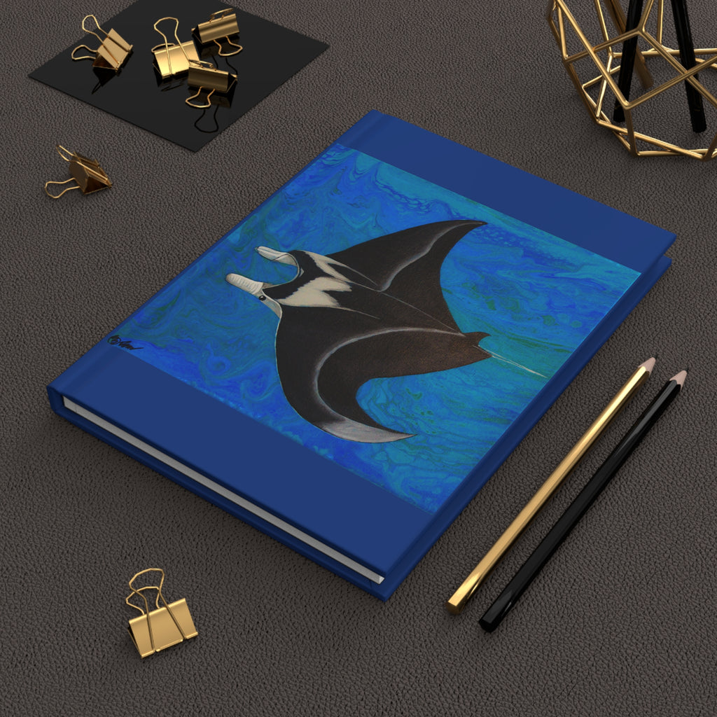 Blue notebook with a manta ray design on a dark surface with stationery items.
