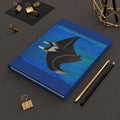 Blue notebook with a manta ray design on a dark surface with stationery items.