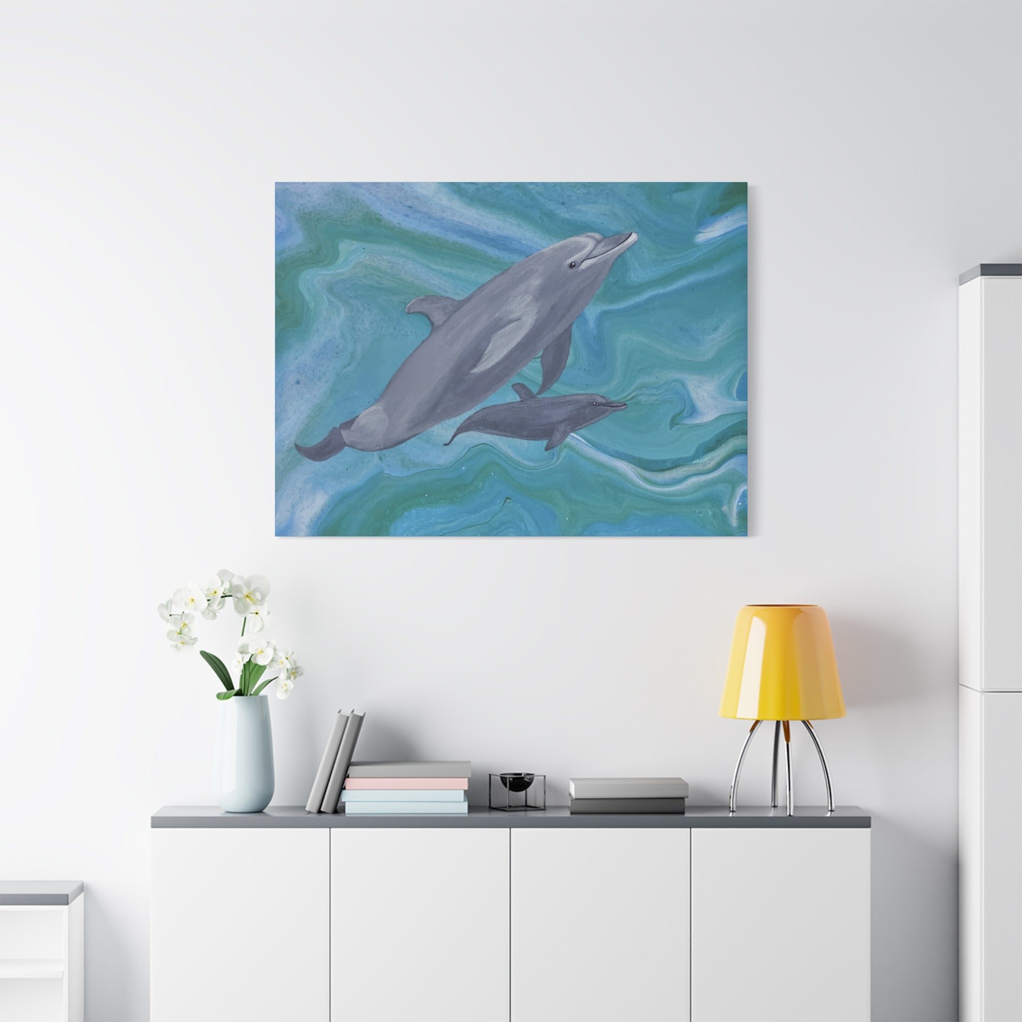 Painting of two dolphins on a wall above a white cabinet with a yellow lamp.