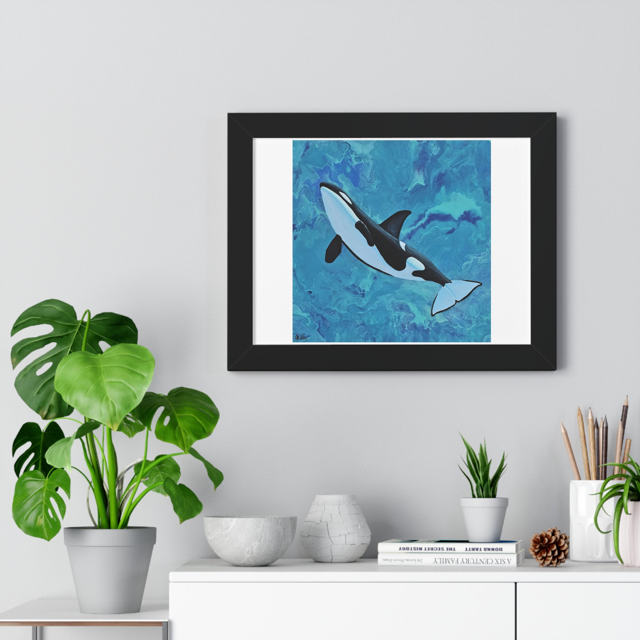Framed artwork of an orca whale on a wall above a white cabinet with decorative items.