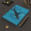 Blue notebook with shark illustration on a dark surface with office supplies