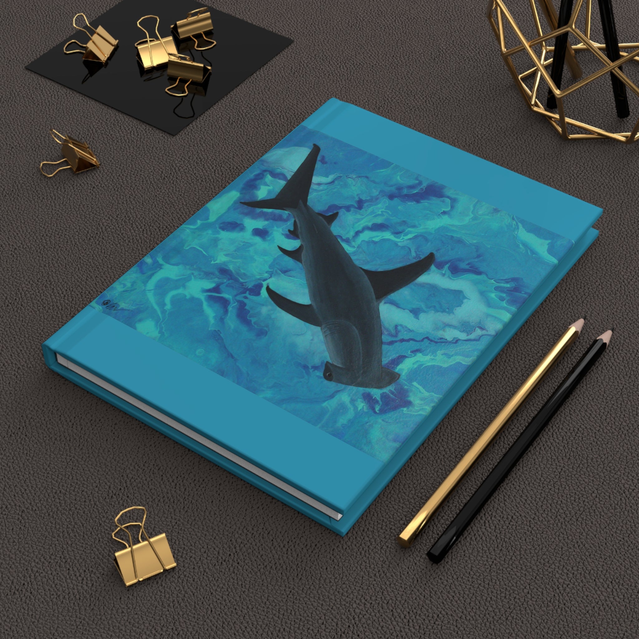 Blue notebook with shark illustration on a dark surface with office supplies