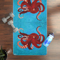 Yoga mat with octopus design on a wooden floor with weights and a water bottle.