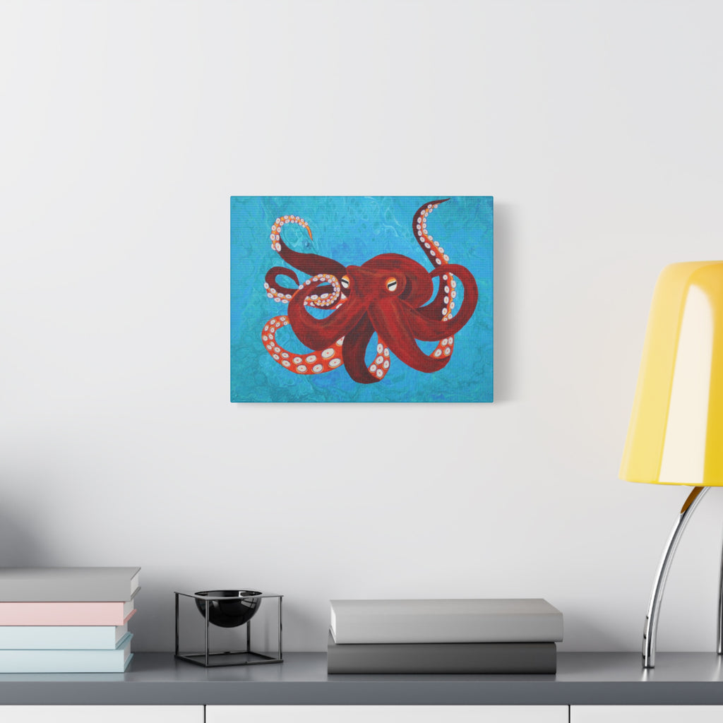 Canvas print of a red octopus on a blue background hanging above a desk with books and a lamp.