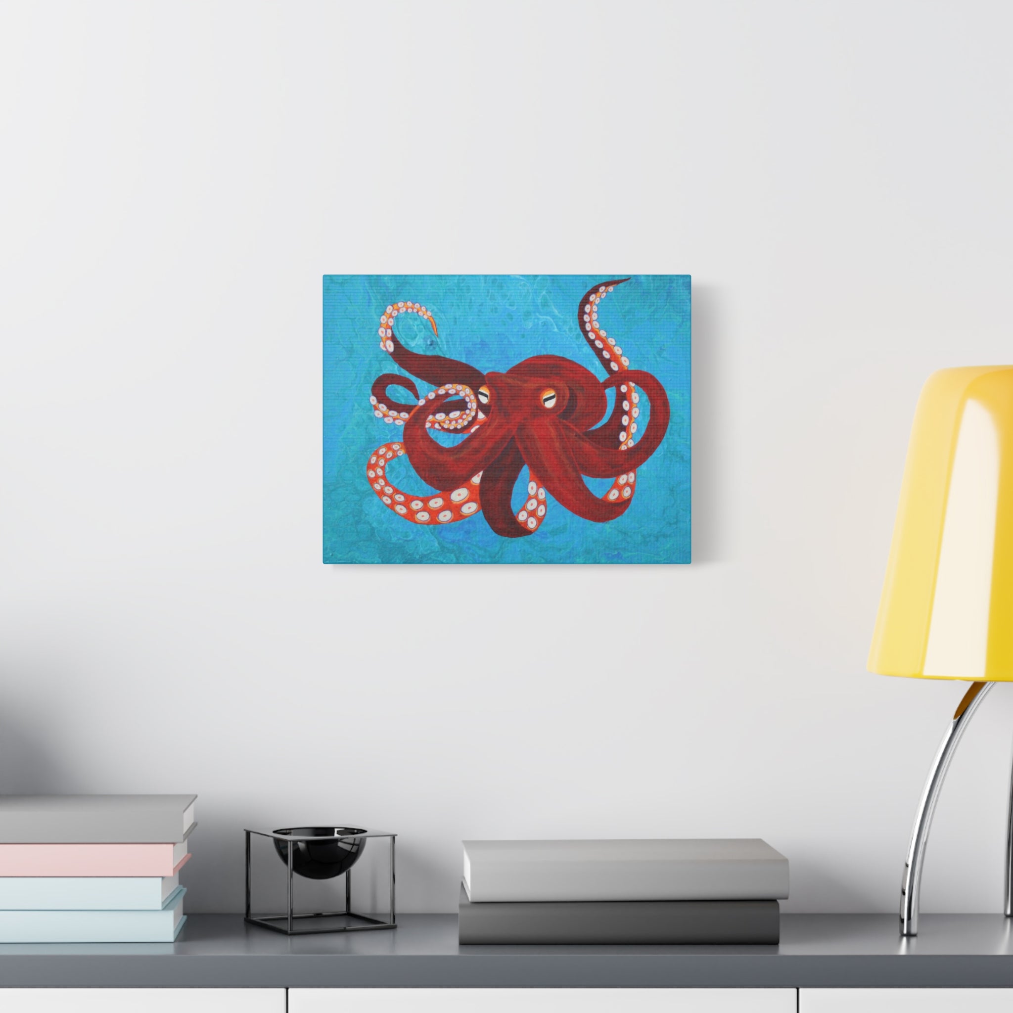 Canvas print of a red octopus on a blue background hanging above a desk with books and a lamp.