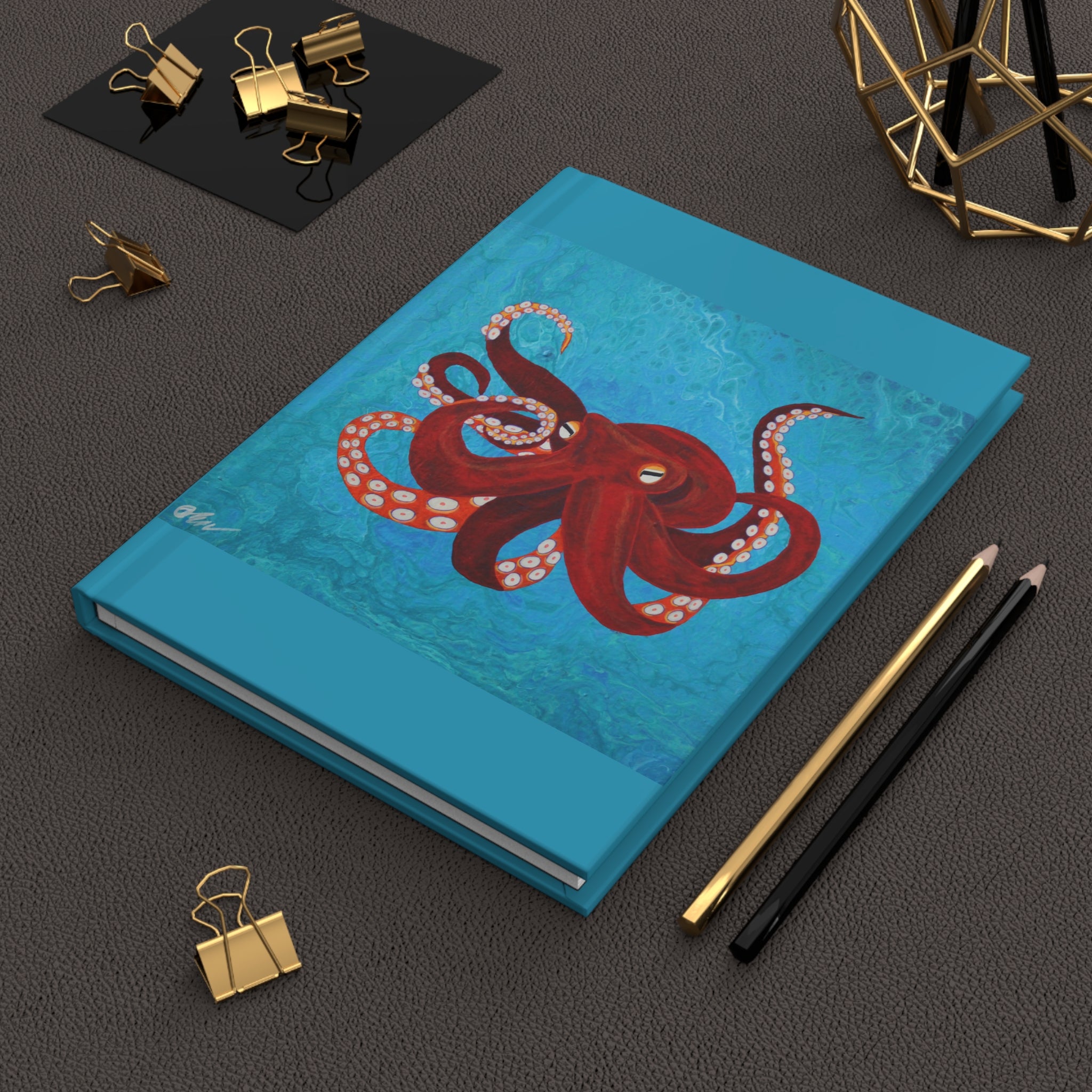 Blue notebook with a red octopus design on a dark surface with stationery items.