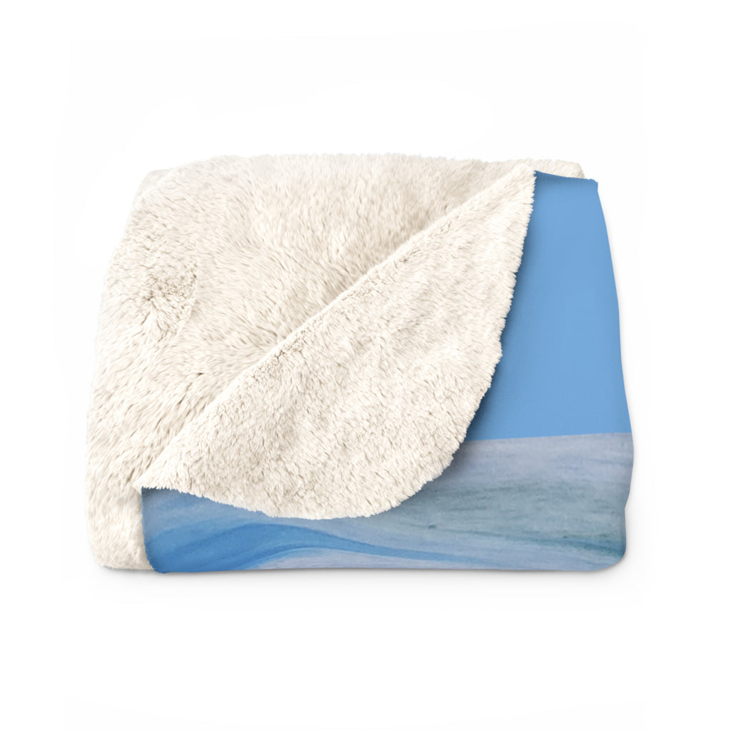 Folded blanket with white sherpa side and blue patterned side on a white background