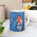 Mug with koi fish design on a coaster, placed on a surface with a plant and container in the background.