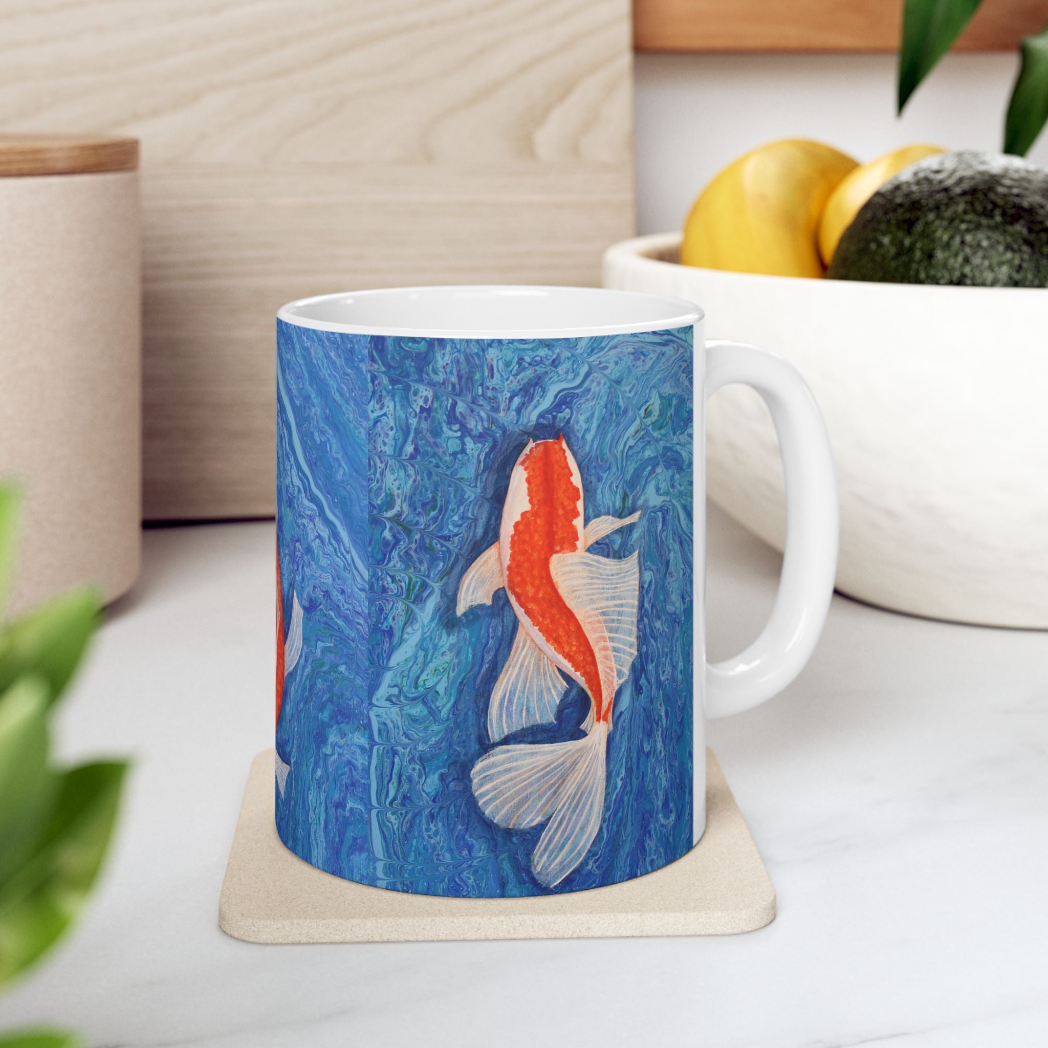 Mug with koi fish design on a coaster, placed on a surface with a plant and container in the background.