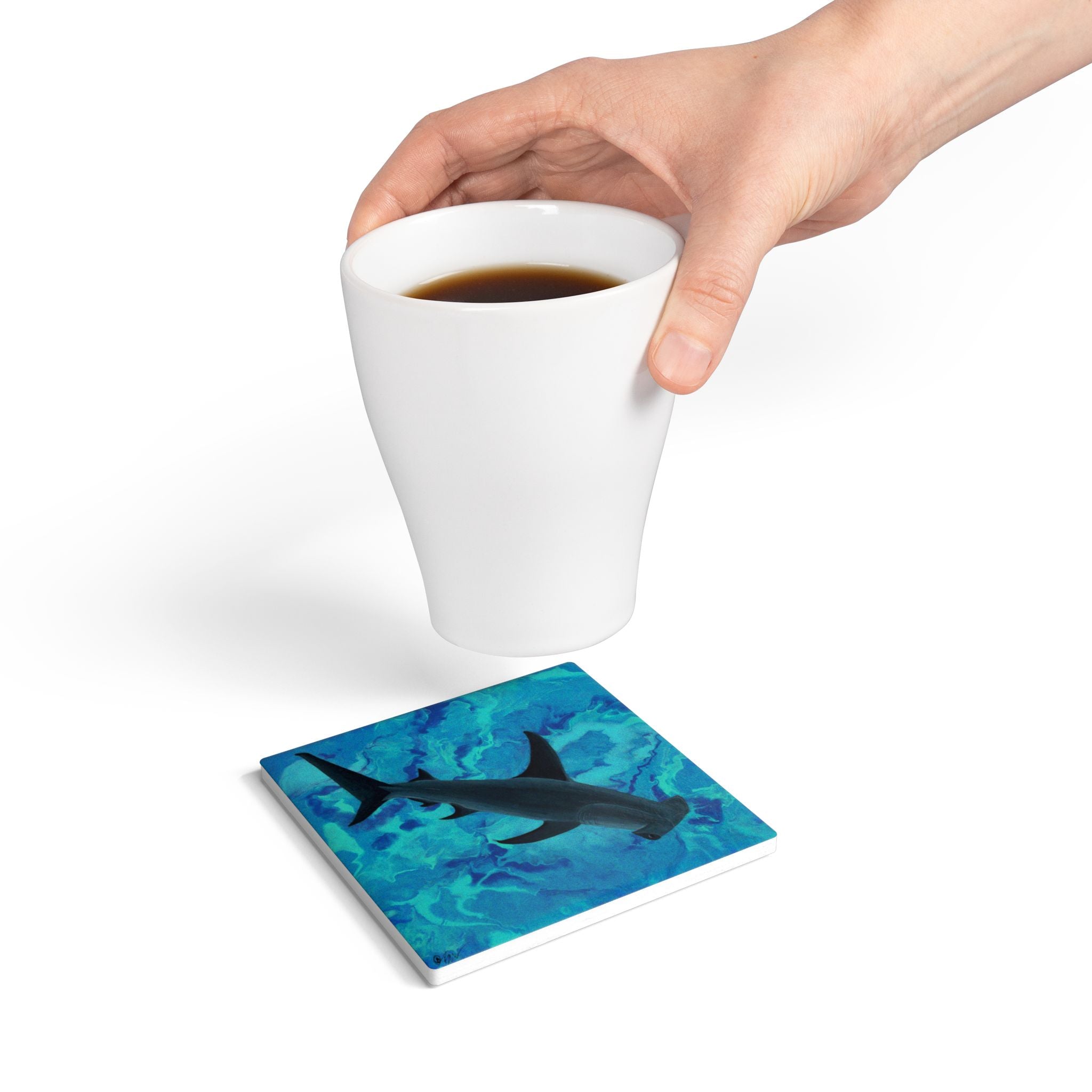 Coaster with shark design on a white surface, hand holding a cup of coffee.