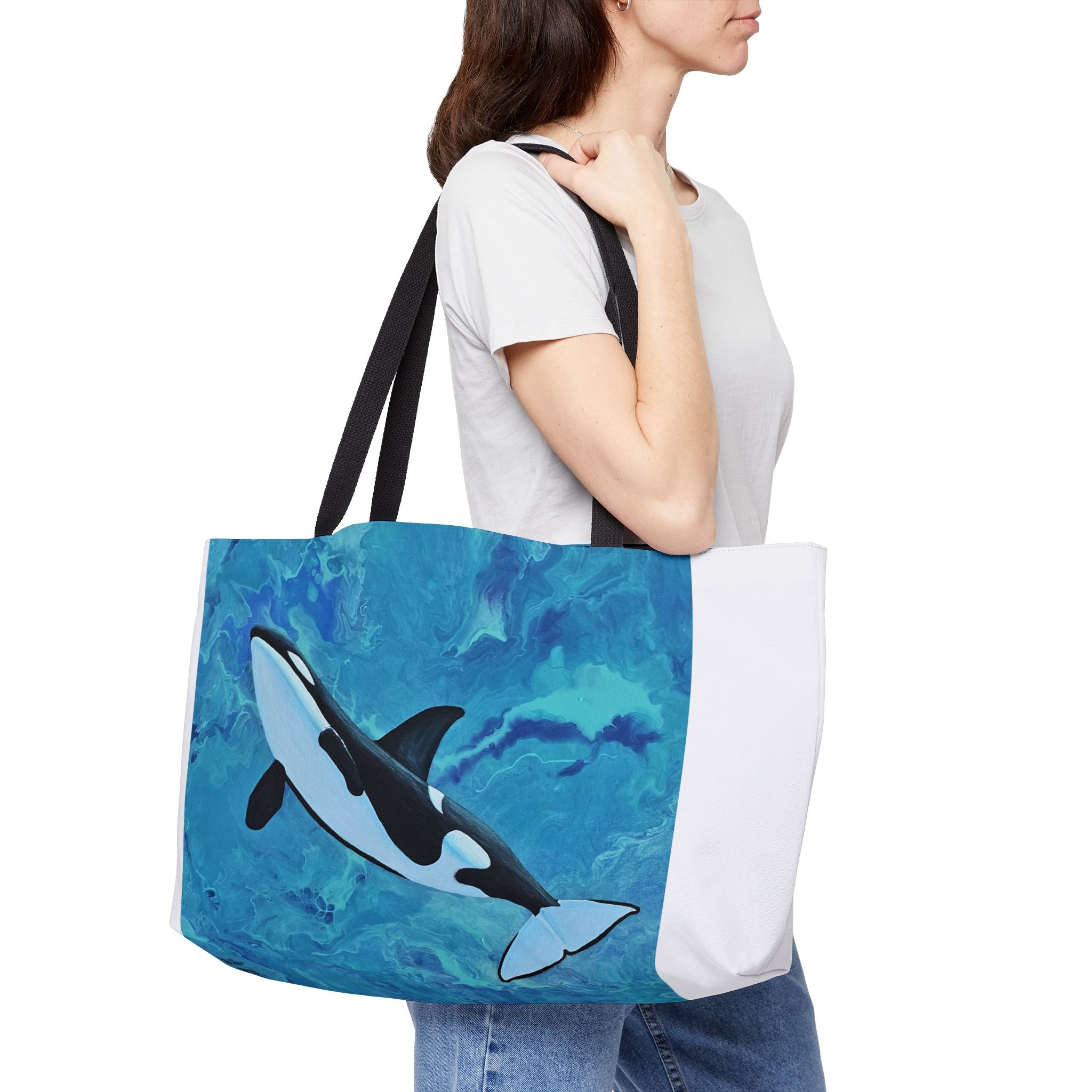 Person holding a tote bag with an orca whale design on a blue and white background