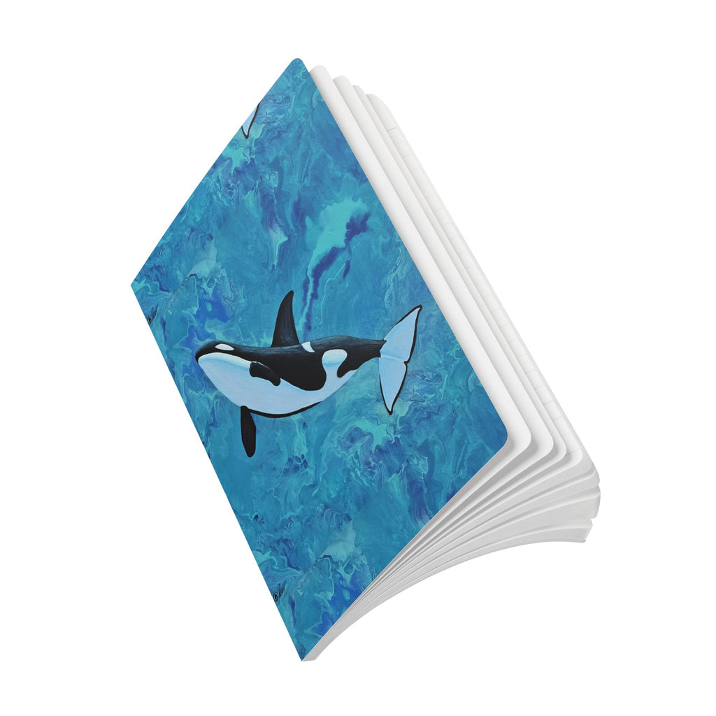 Notebook slightly open with an orca whale design on a blue watercolor background