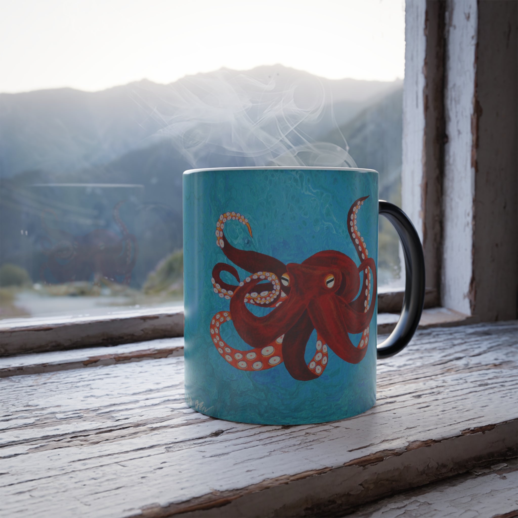 Teal mug with an octopus design on a wooden surface with a mountain view.