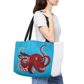 Person holding a tote bag with a red octopus design on a blue background