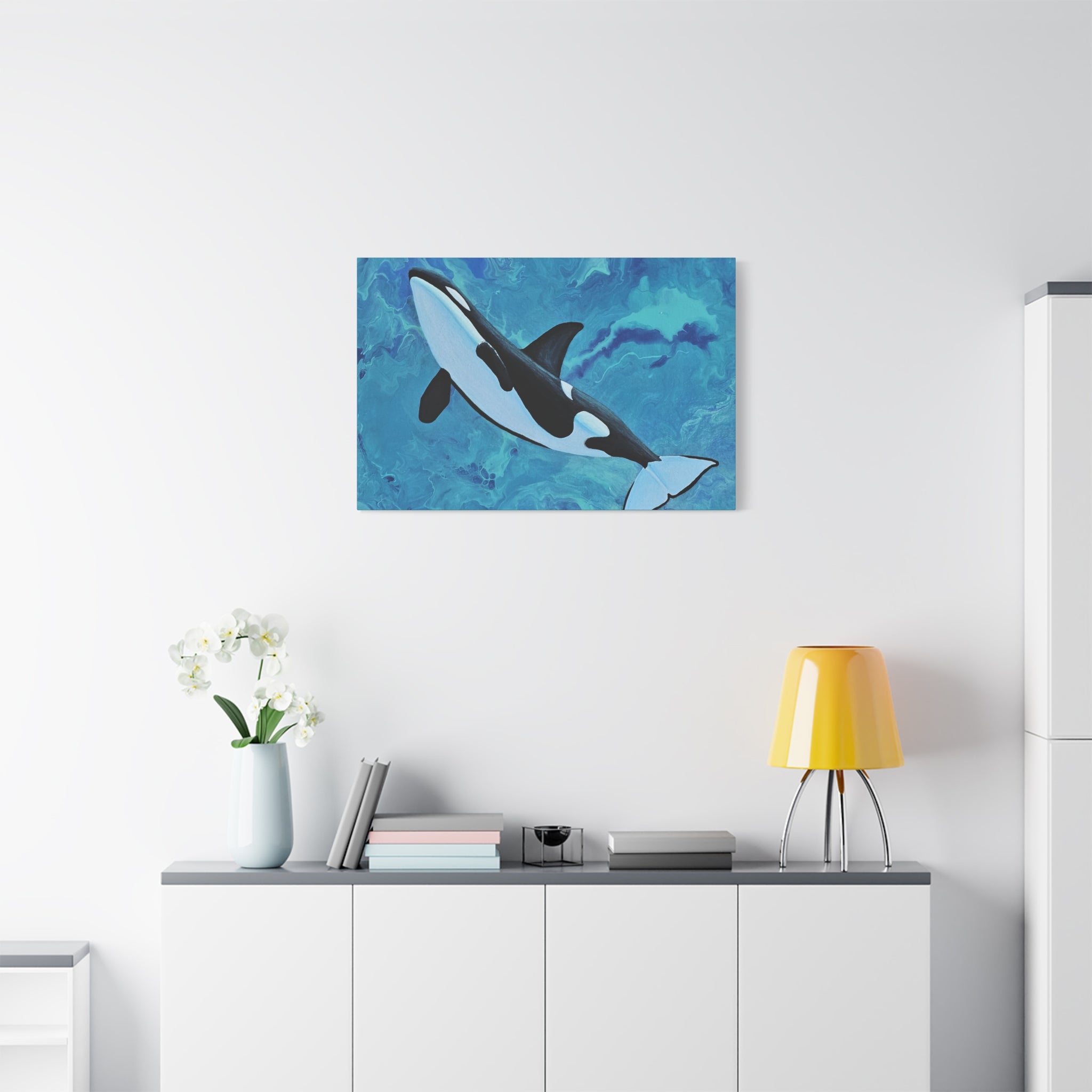 Orca whale painting on a wall above a white cabinet with a yellow lamp.