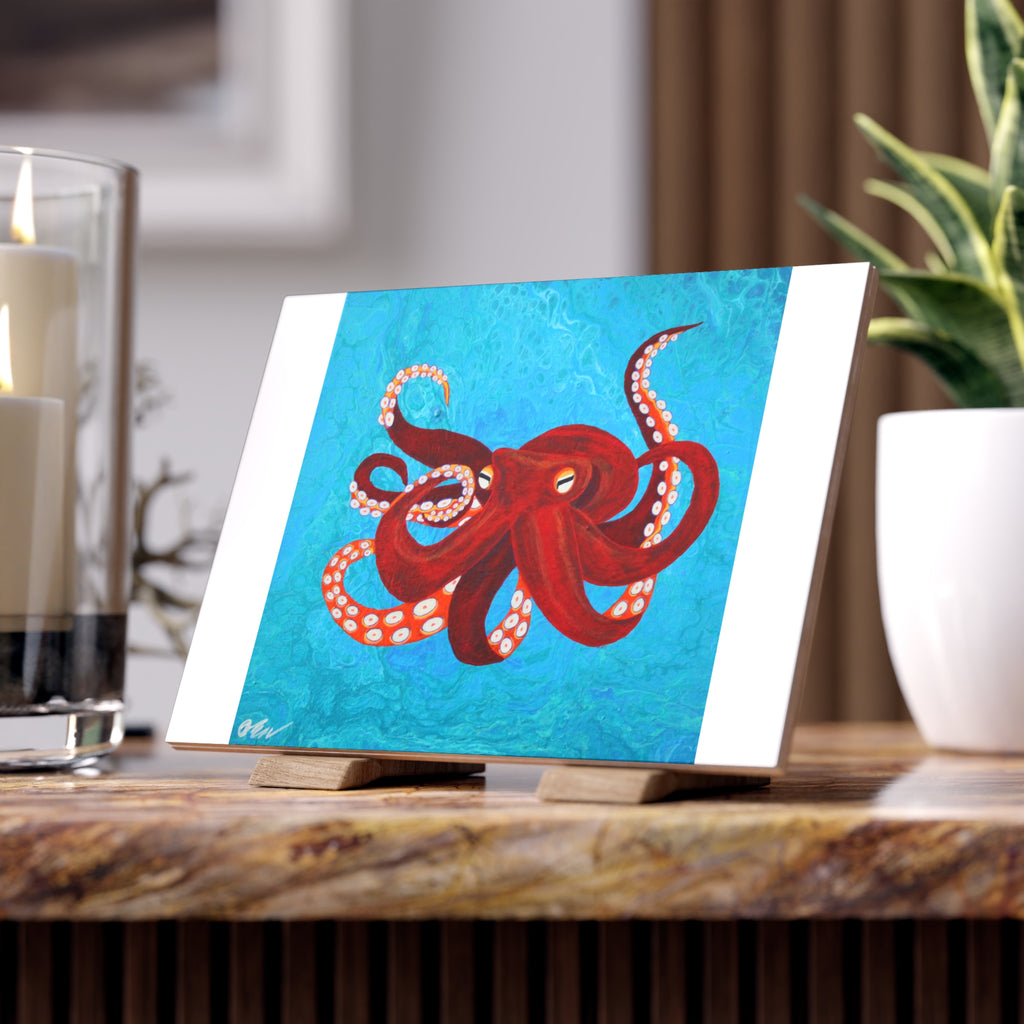 Tile with a red octopus design on a blue background, placed on a wooden surface.