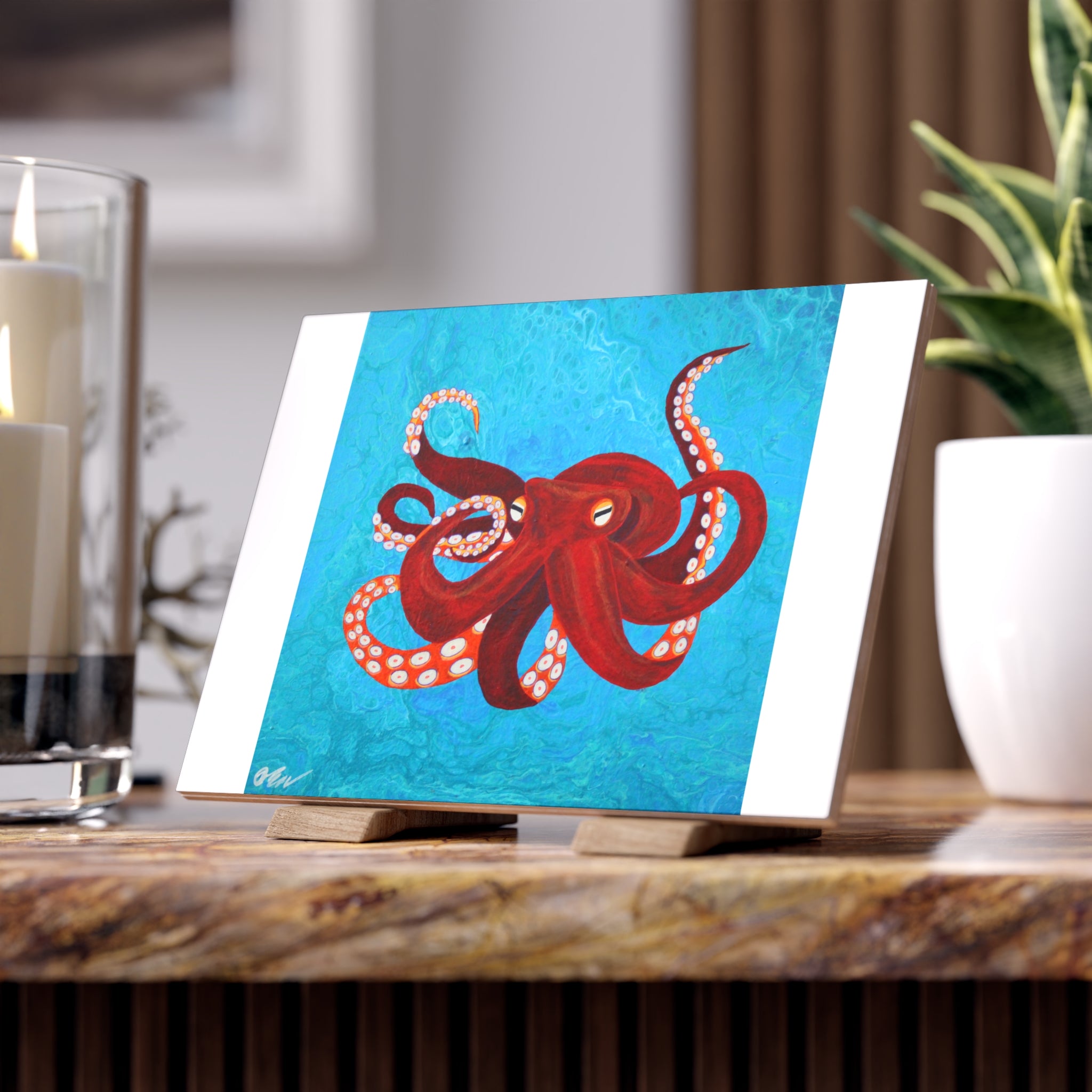 Tile with a red octopus design on a blue background, placed on a wooden surface.