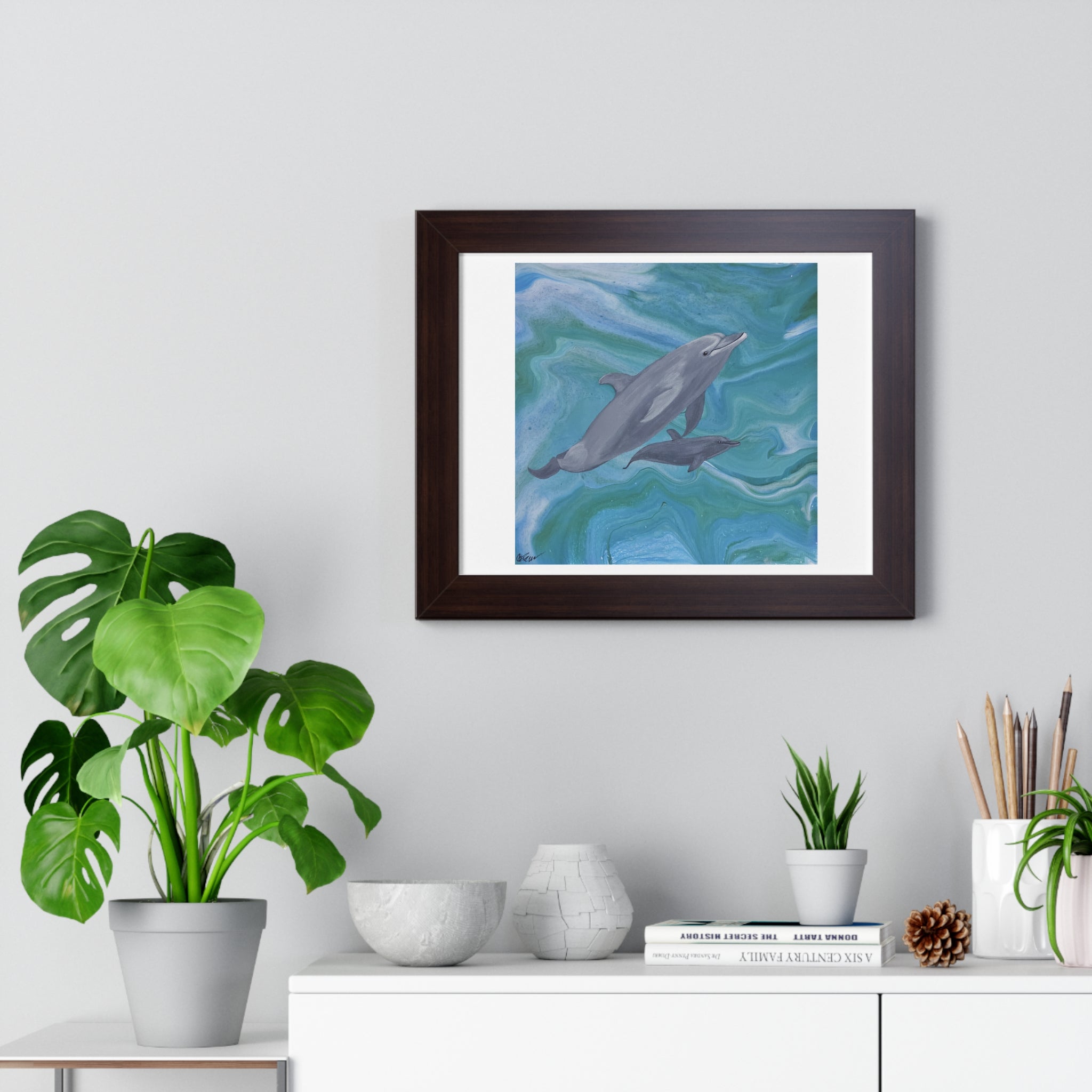 Framed artwork of dolphins on a wall above a white cabinet with decorative items.