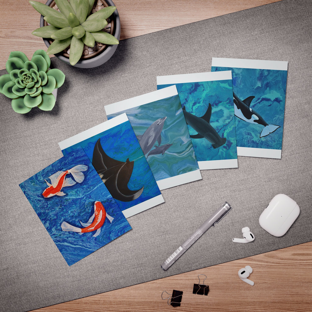Set of greeting cards with ocean-themed designs on a desk with office supplies.