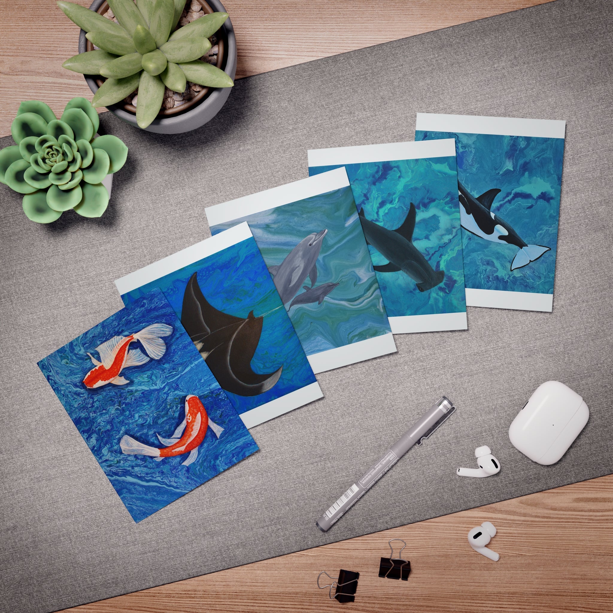 Set of greeting cards with ocean-themed designs on a desk with office supplies.