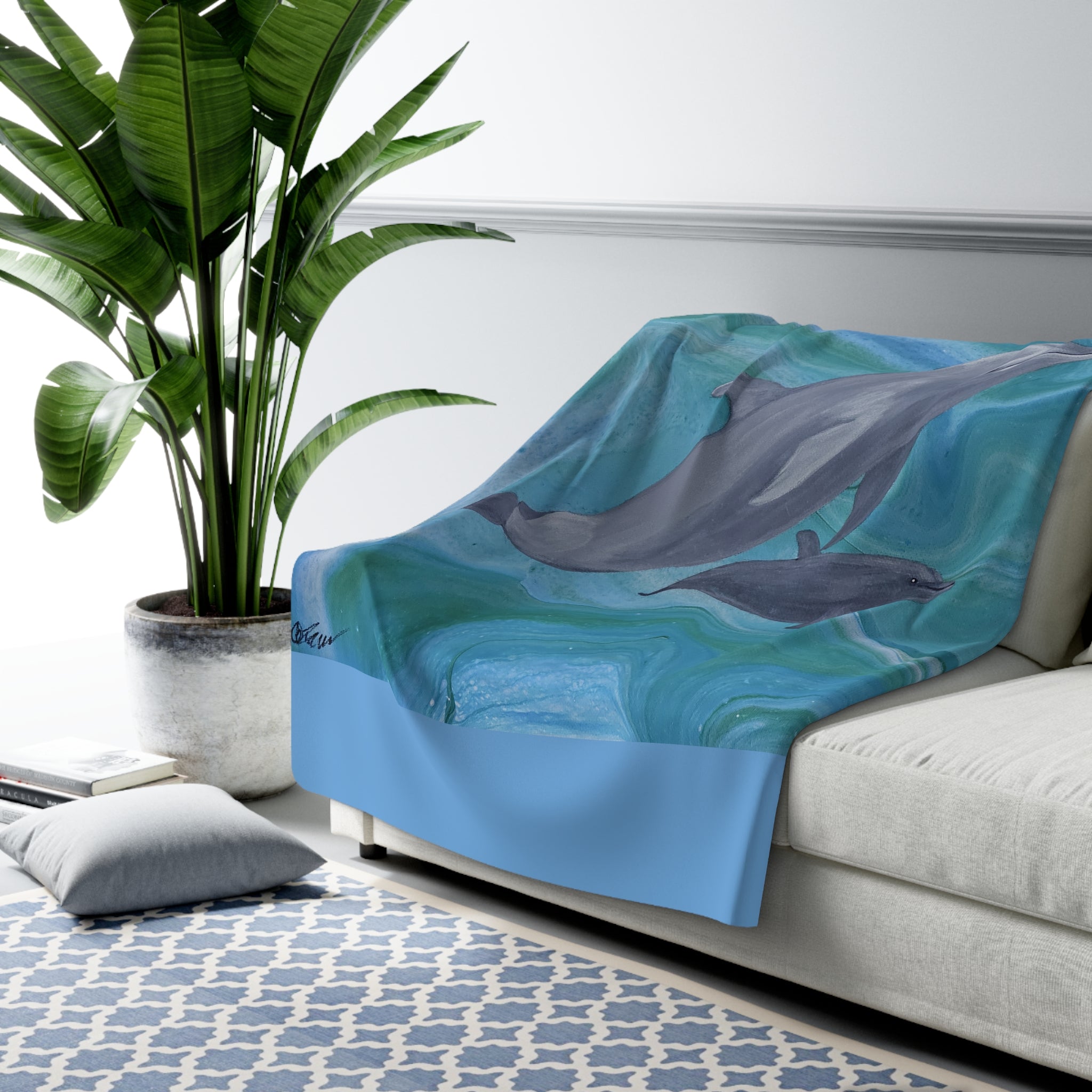 Couch with a blue blanket featuring dolphins, next to a potted plant in a living room.
