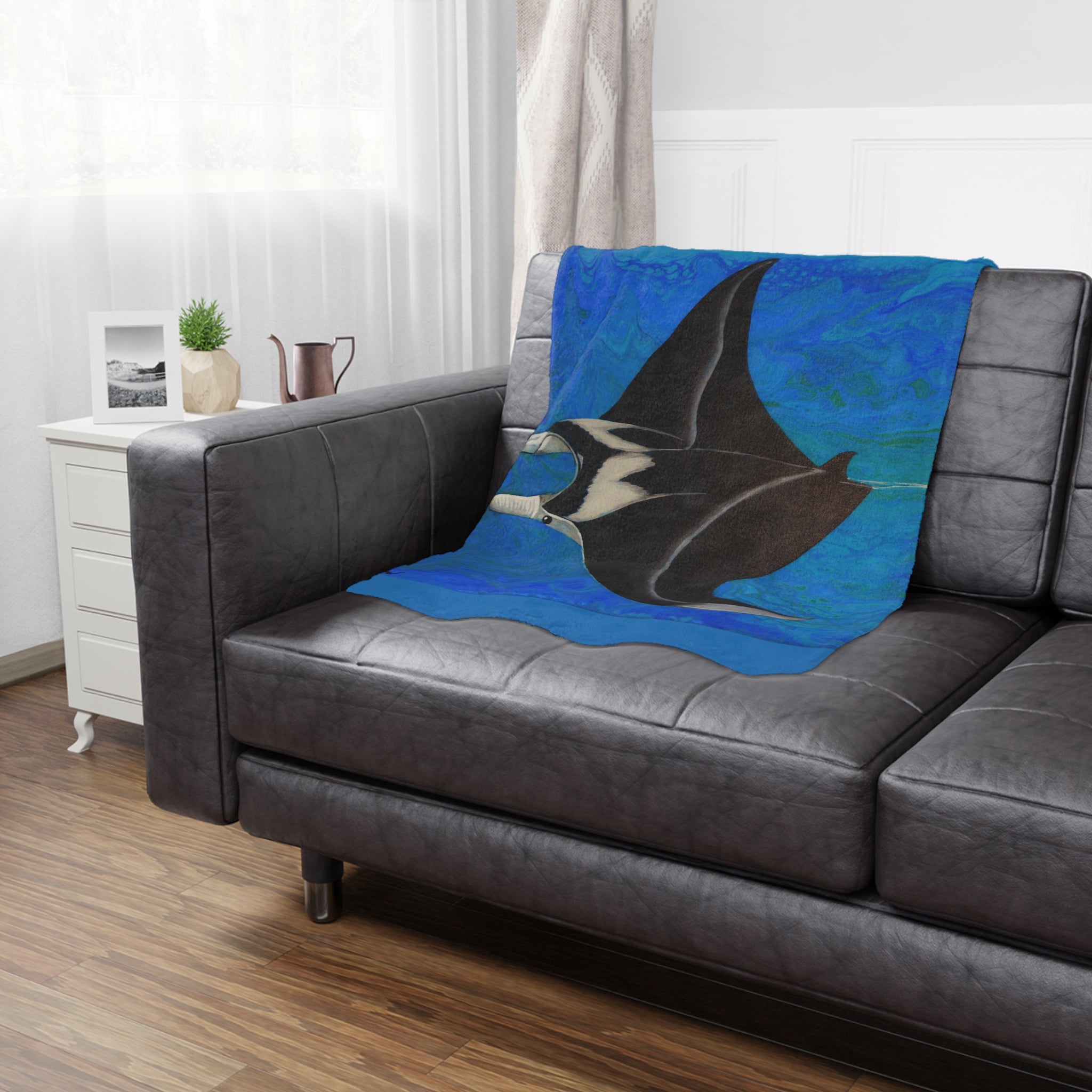 Gray sofa with a decorative blanket featuring a manta ray design on a blue background.