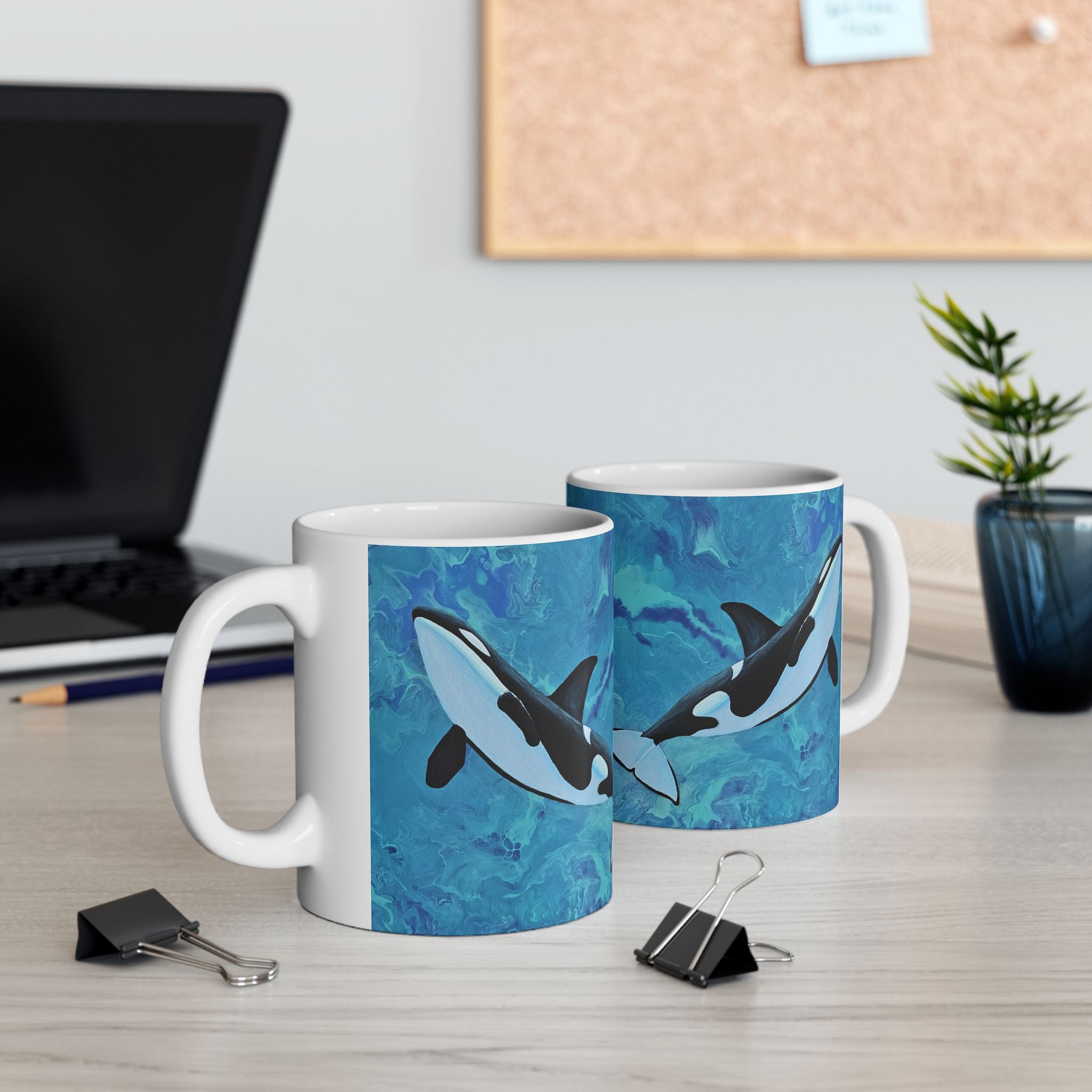 Two mugs with shark designs on a desk with office supplies and a plant.