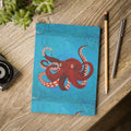 Notebook with a red octopus design on a wooden surface with a pen and pencil.