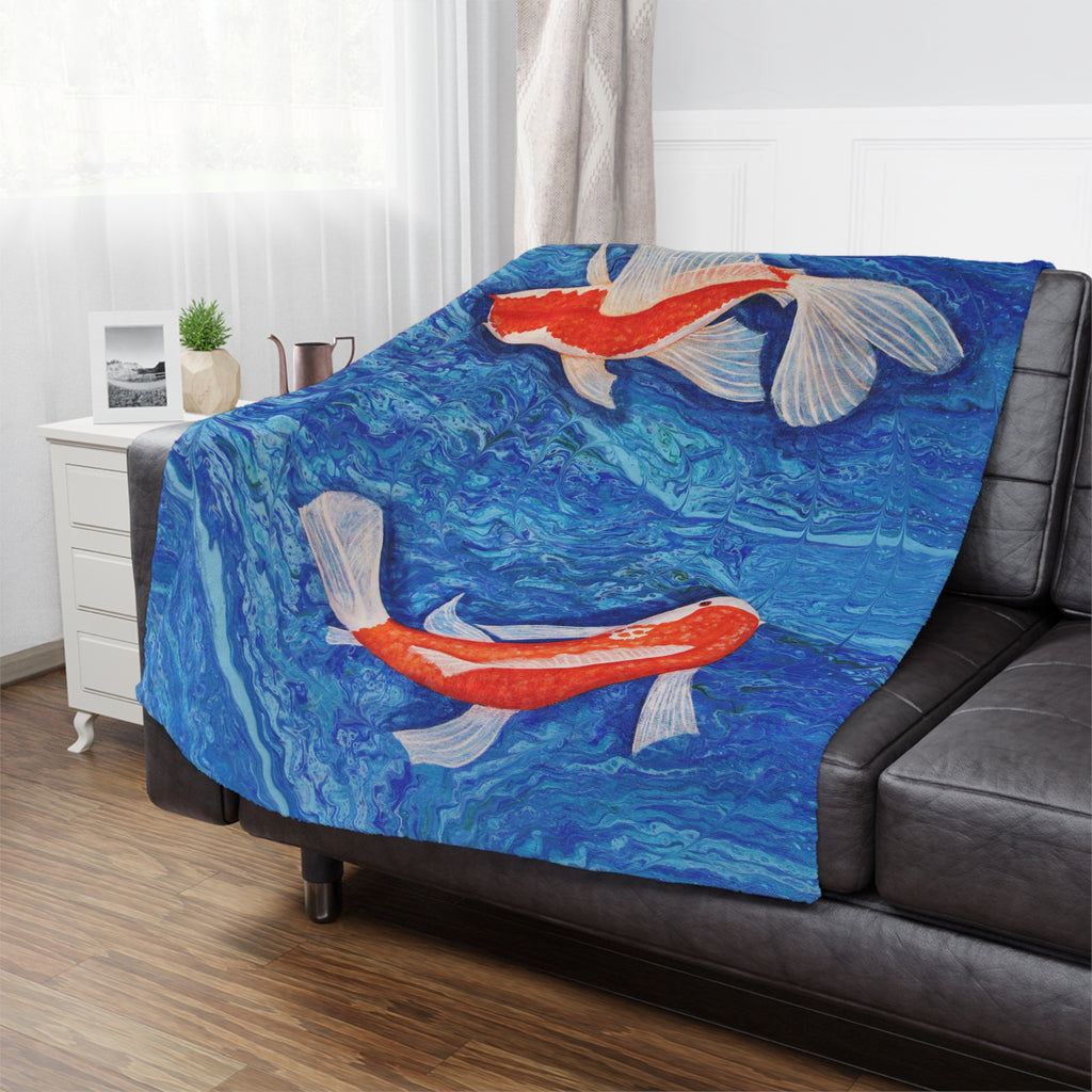 Blue blanket with Koi fish design draped over a black sofa in a room.