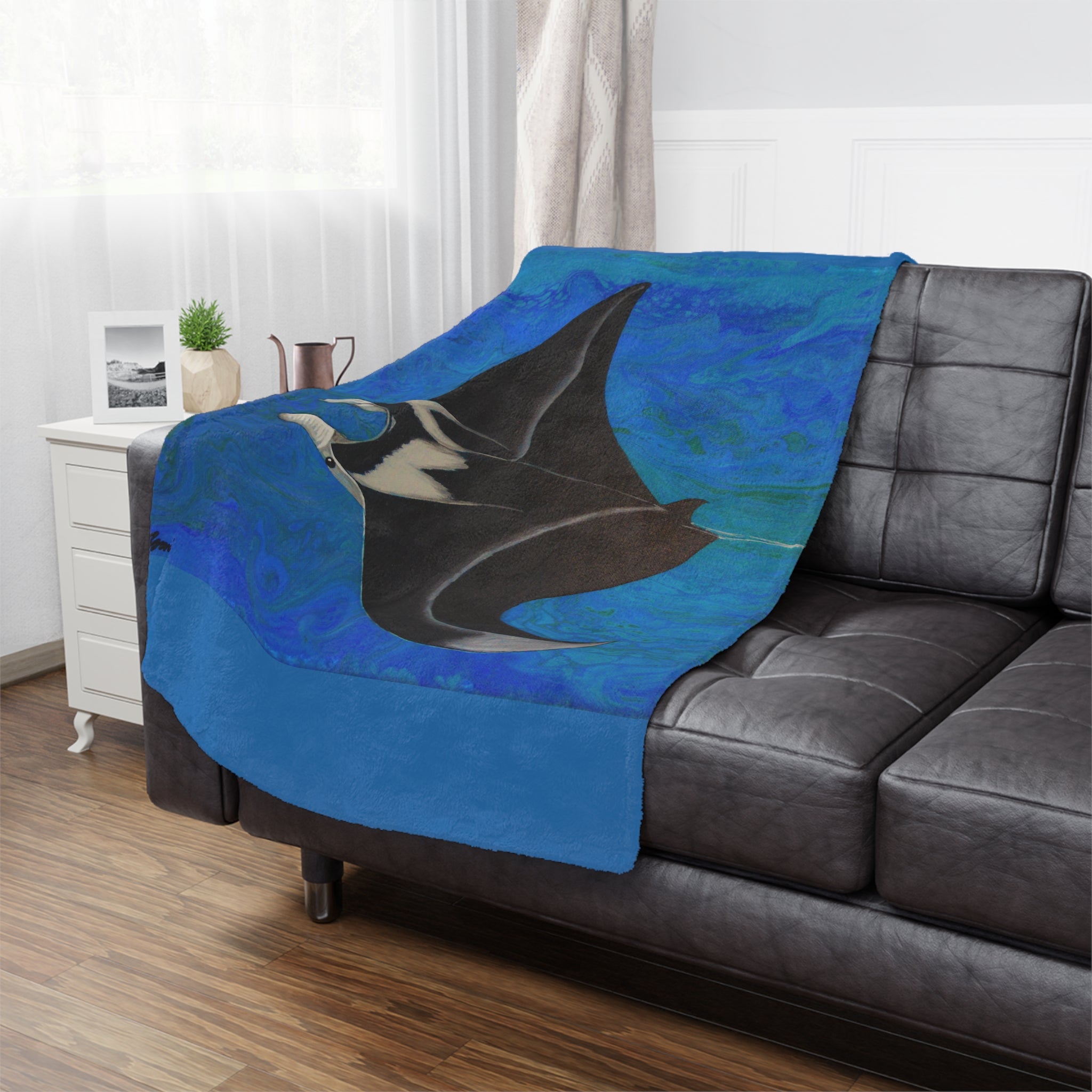 Blue blanket with a manta ray design draped over a gray sofa in a living room.