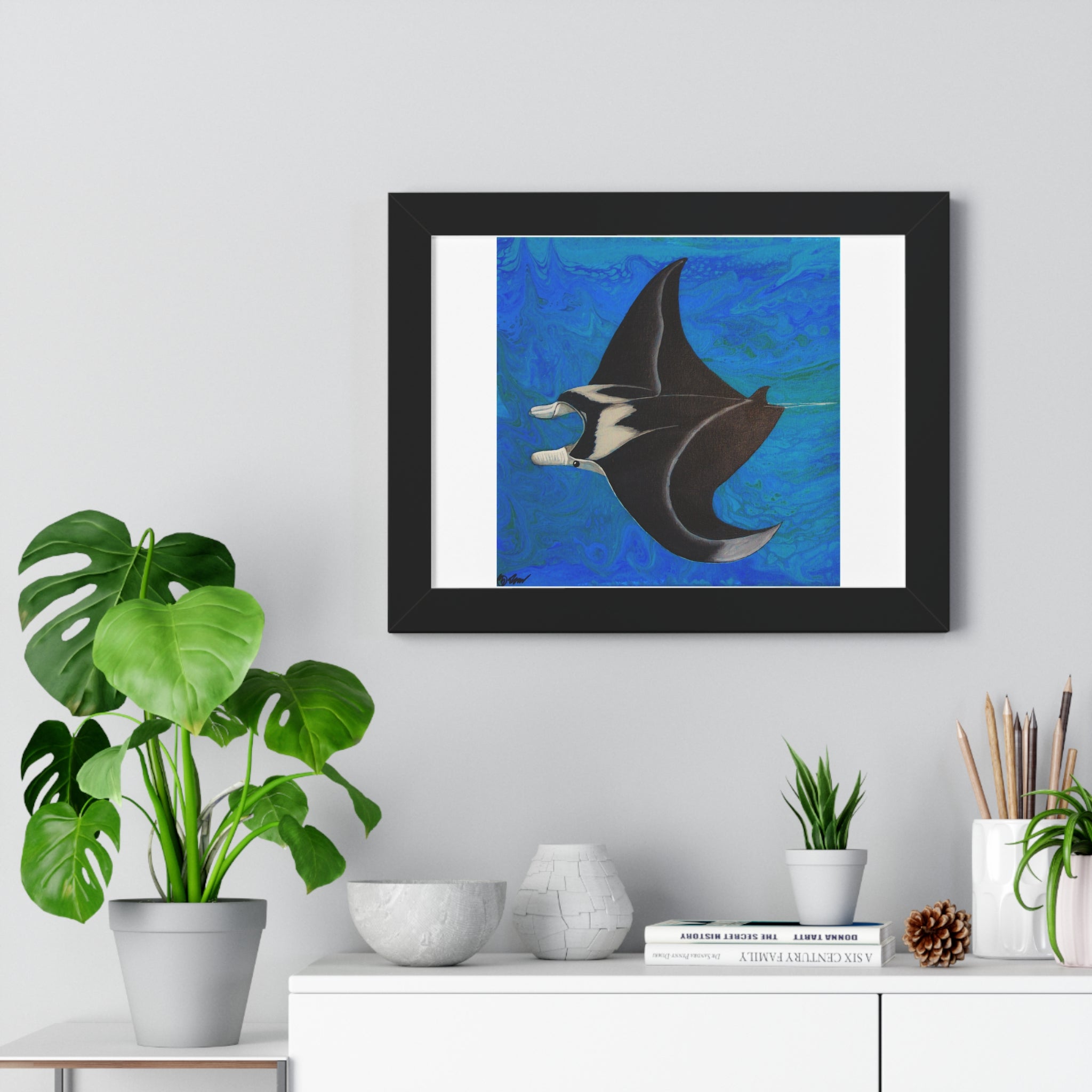 Framed artwork of a manta ray on a wall above a white cabinet with decorative items.
