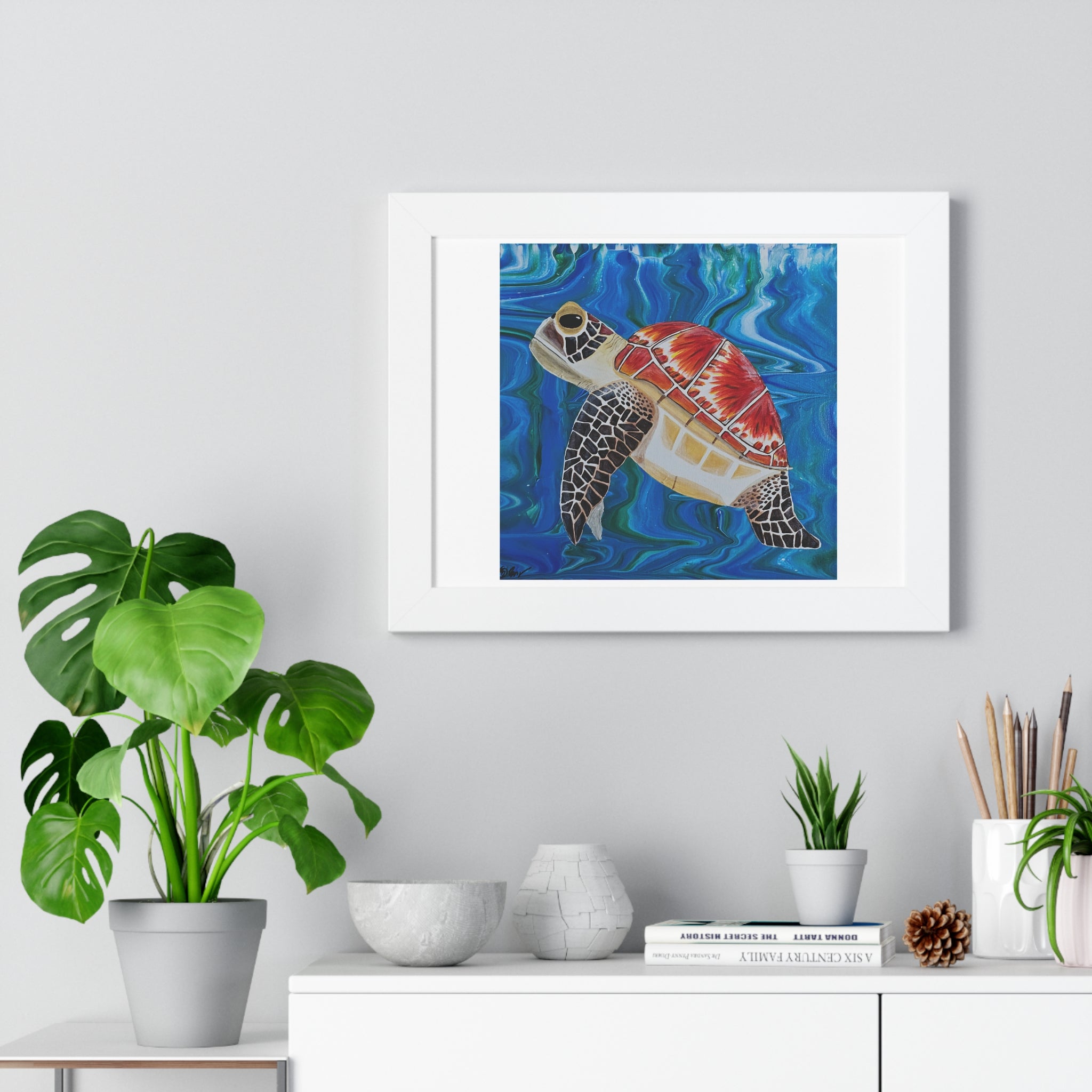 Framed artwork of a colorful turtle in an underwater scene, placed on a shelf with decorative items.